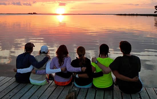 Students sitting on a dock looking at the sunset