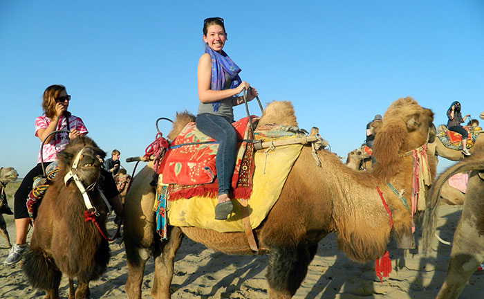 Students smile atop saddled camels as they get ready for a tour
